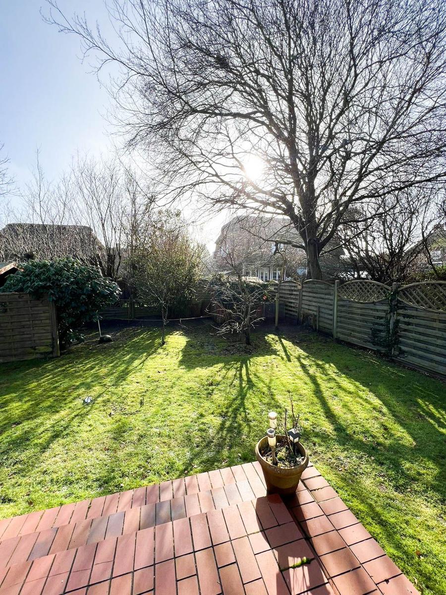 Hinterhof mit Rasenfläche, Terrasse und einem großen Baum. Holzzaun umgibt den Garten.