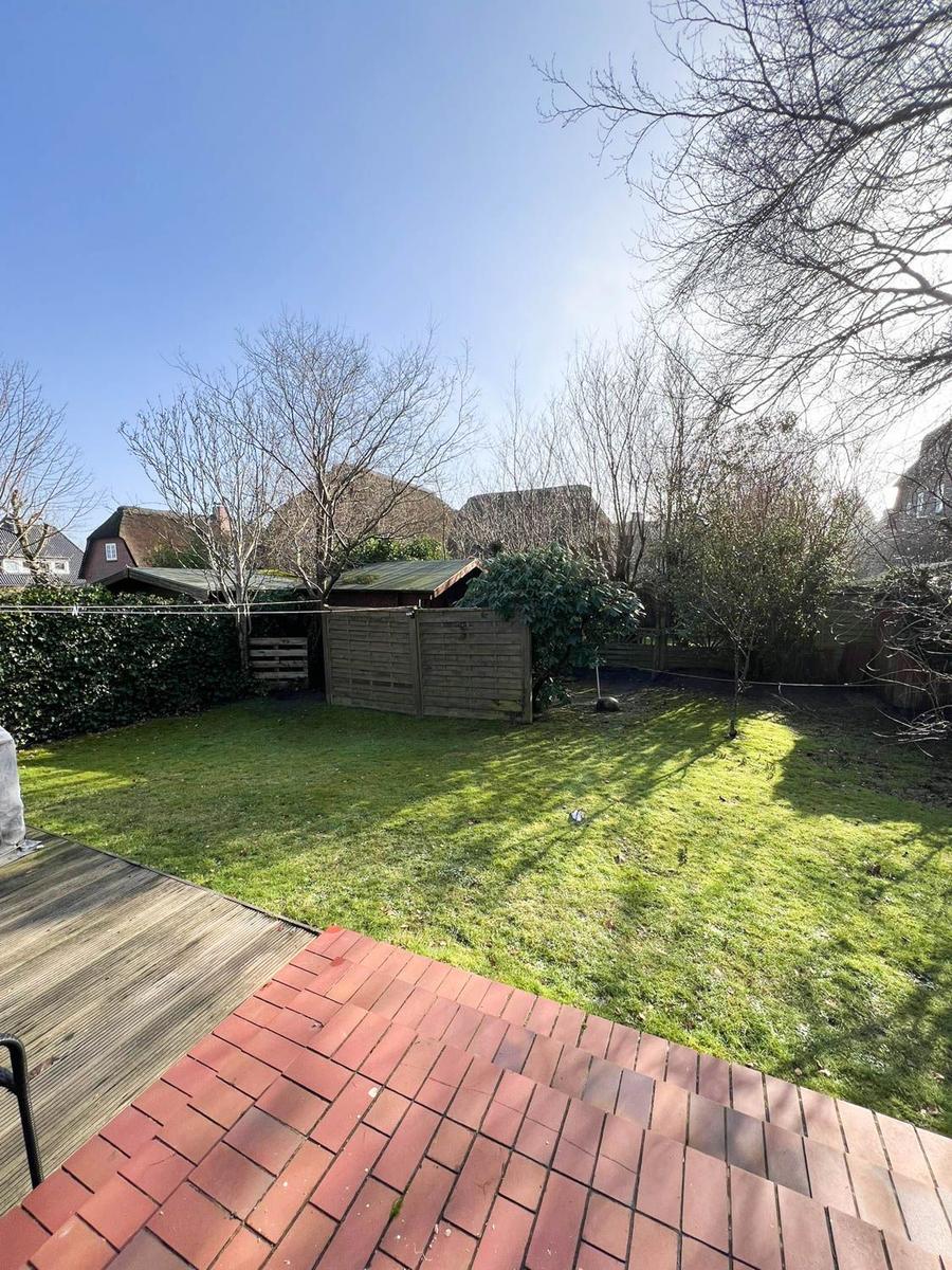 Hinterhof mit Rasenfläche, Holzterrasse und Gartenzaun. Bäume ohne Blätter im Hintergrund.