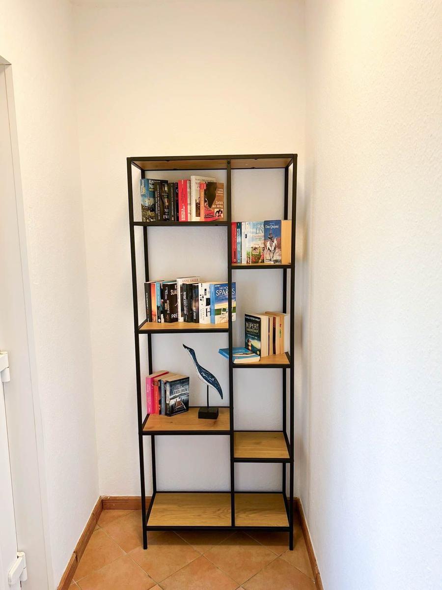 Höhenregal mit Büchern und Vogeldekoration in einem Raum mit Terrakottaboden.