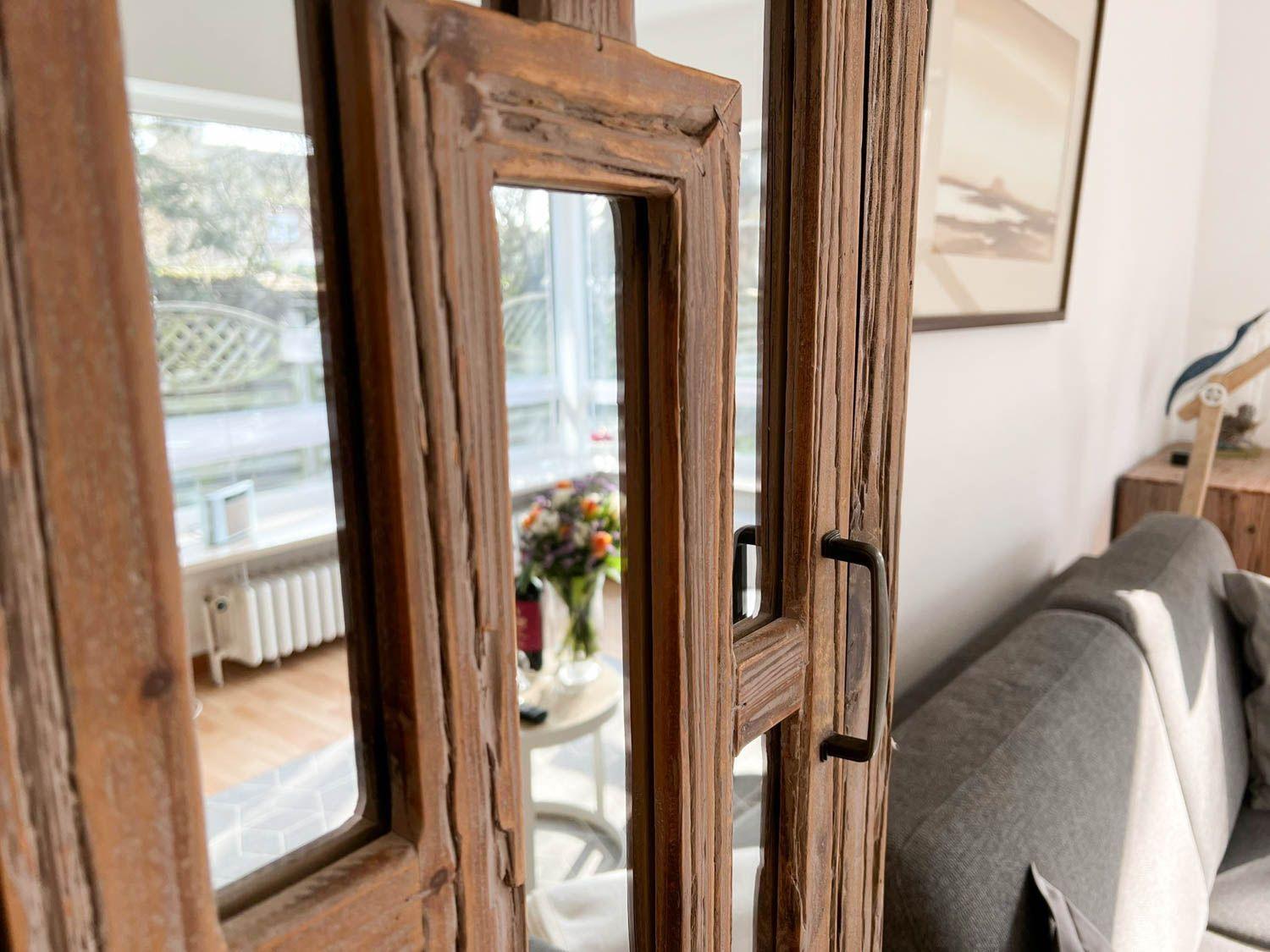 Durch eine alte Holztür blickt man in einen Raum mit Sofa und Blumen.