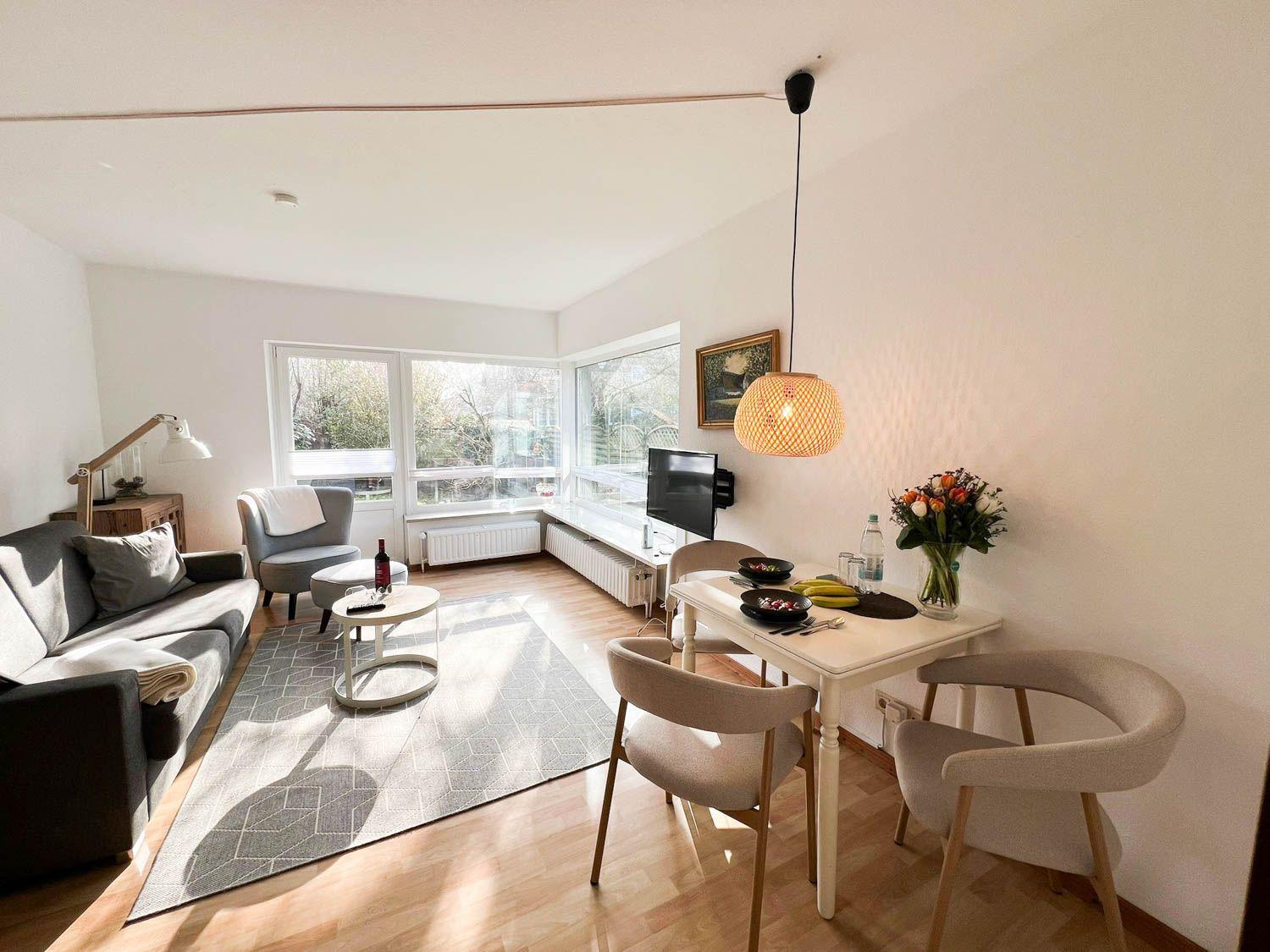 Wohn- und Essbereich mit Sofa, Tisch und Stühlen. Fenster bieten Blick auf Garten.