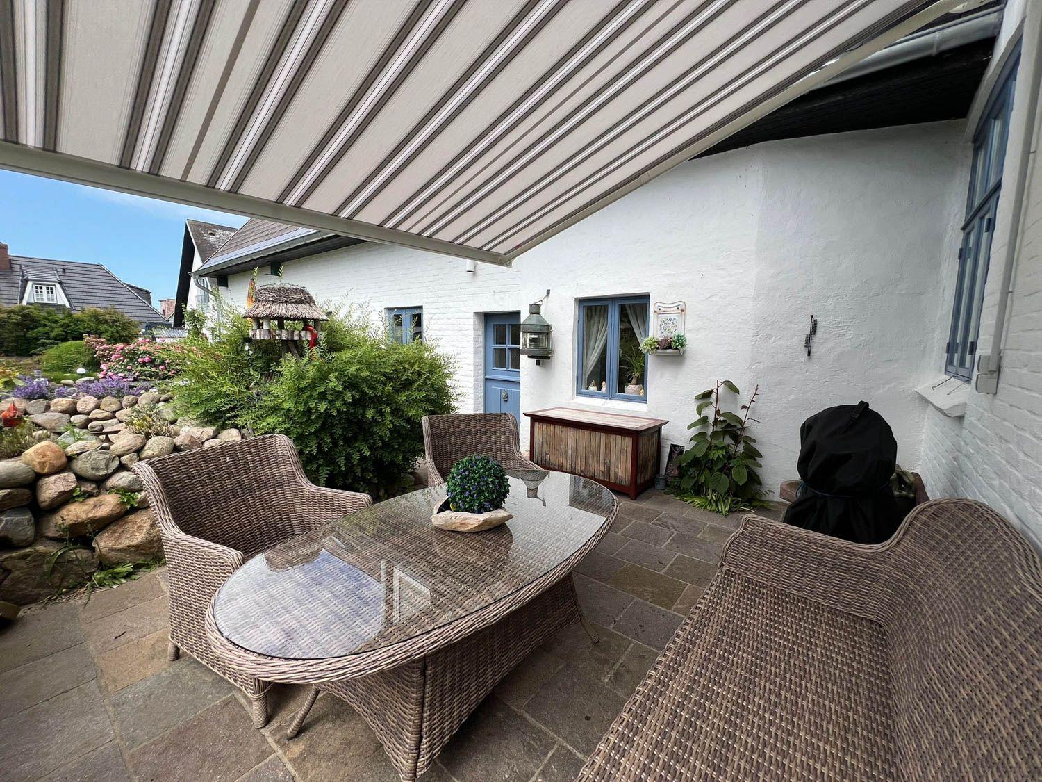 Terrasse mit Sitzgruppe unter Markise, weiße Hauswand und Garten mit Steinmauer.