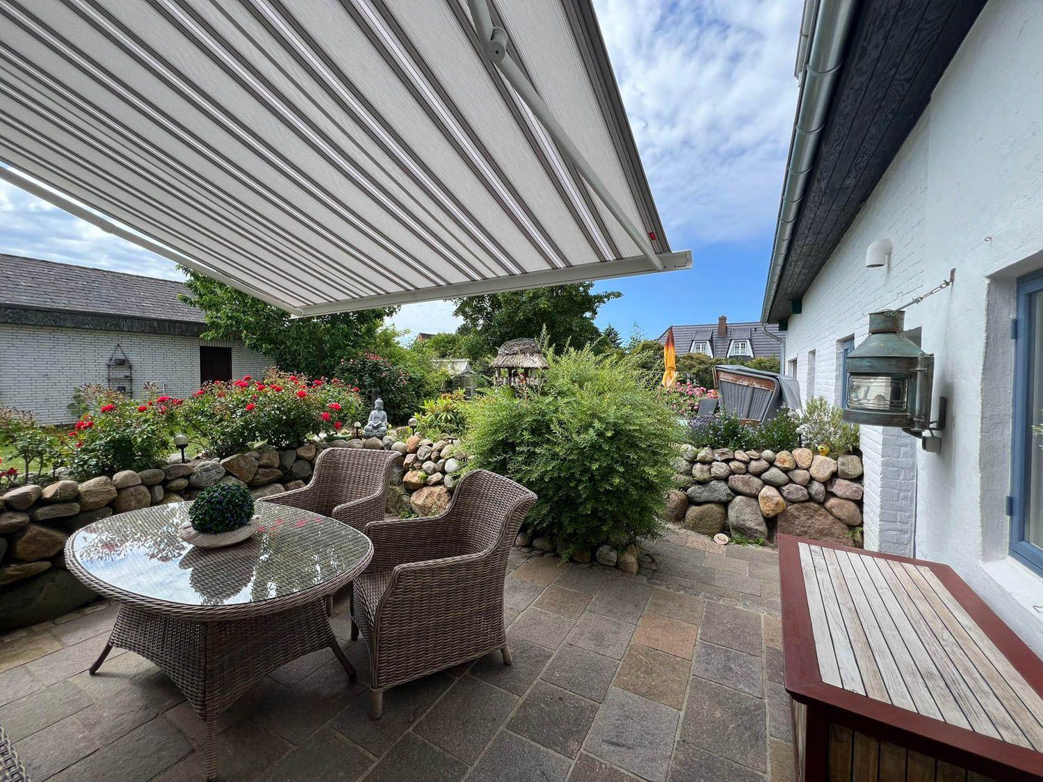 Terrasse mit Markisen, Gartenmöbeln und Steinmauer. Hinterhof mit Pflanzen und Steinweg.