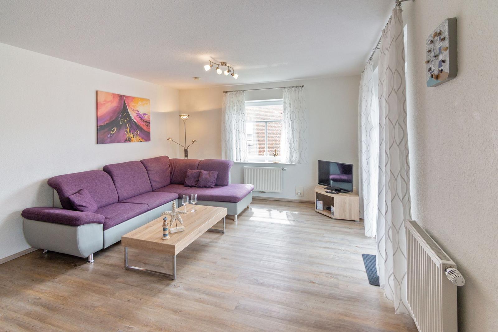 Wohnzimmer mit L-förmigem Sofa, Couchtisch und Fernseher.