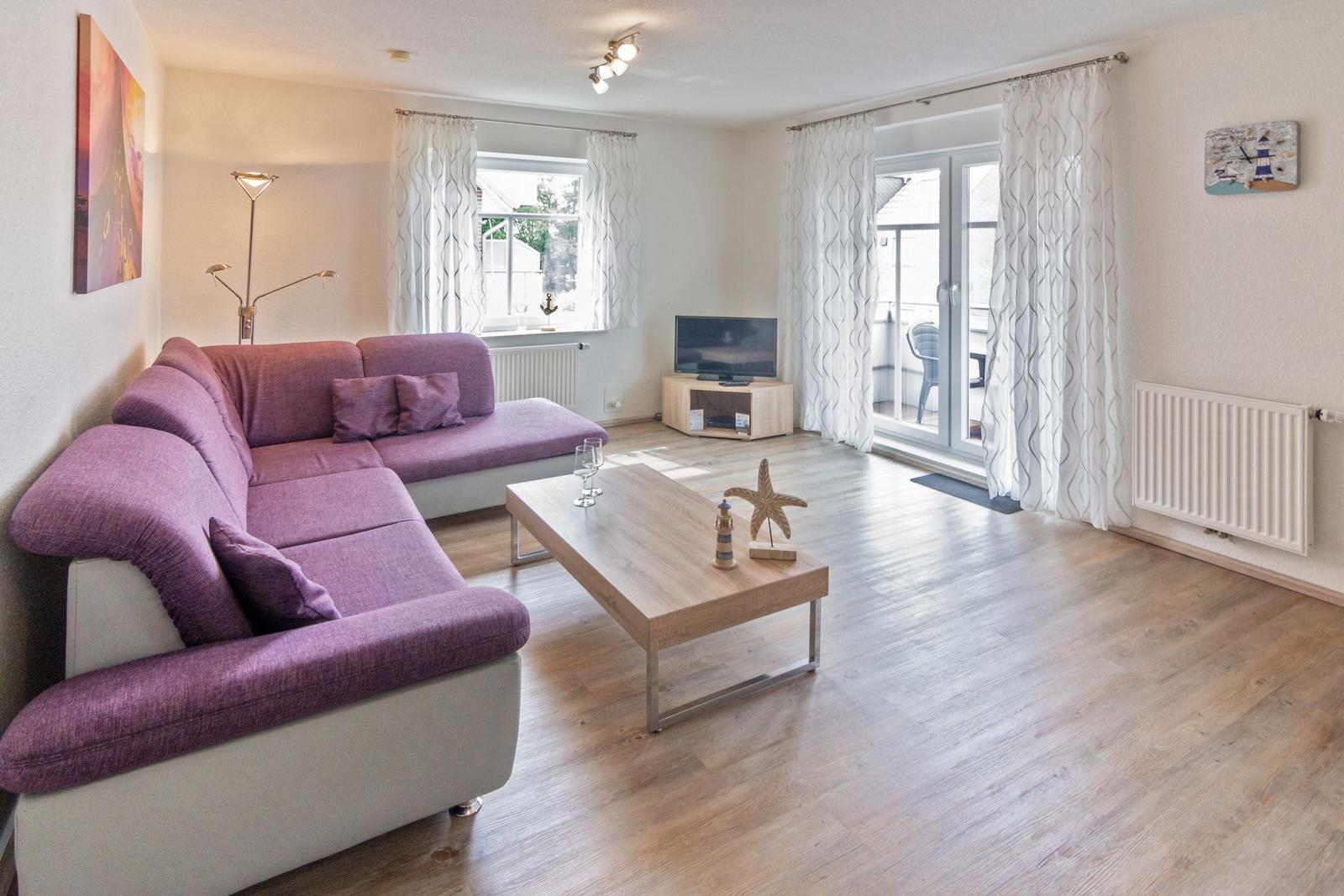 Wohnzimmer mit lila Sofa, Holztisch und TV. Durchgang zur Terrasse.