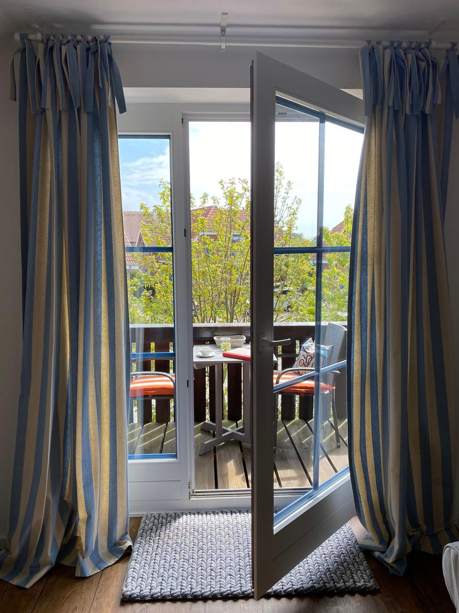Durchgehende Glastüren führen auf eine Terrasse mit Tisch und Stühlen. Vorhänge sind blau-creme gestreift.