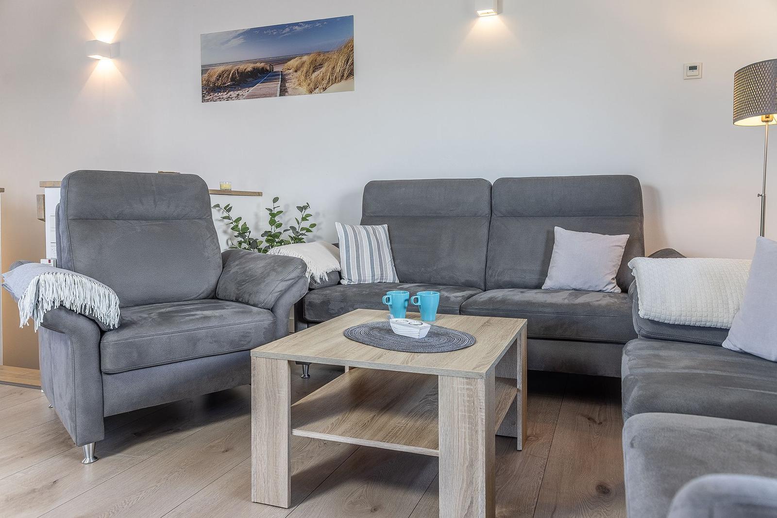 Living room with gray sofa, armchair, and wooden table. Wall art and floor lamp are visible.