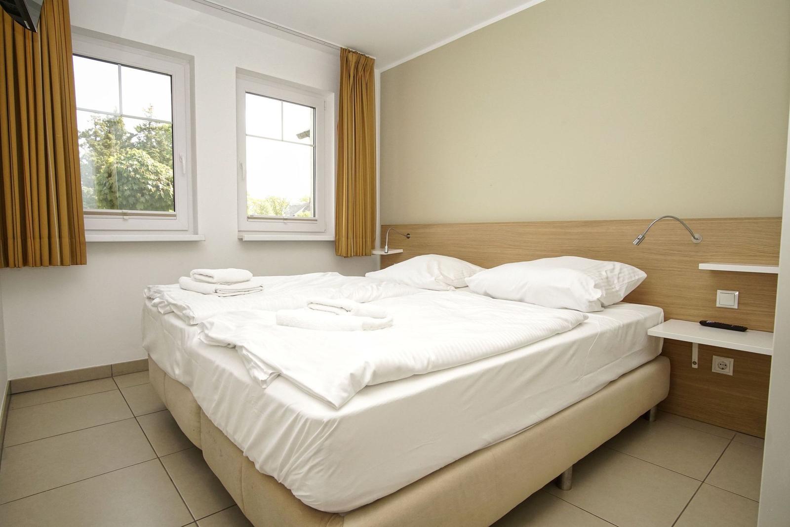 Ein Schlafzimmer mit Doppelbett, zwei Fenstern und Holzverkleidung an der Wand.
