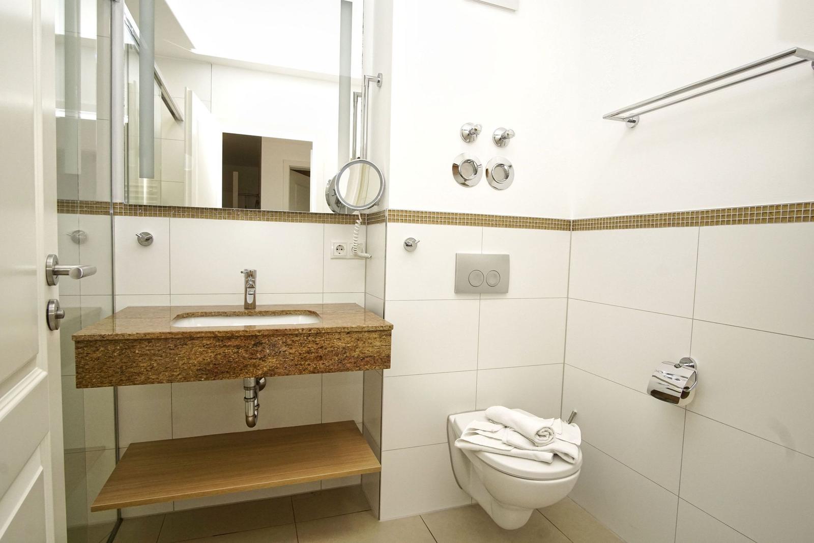 Badezimmer mit Waschtisch, Spiegel, Toilette und Dusche.