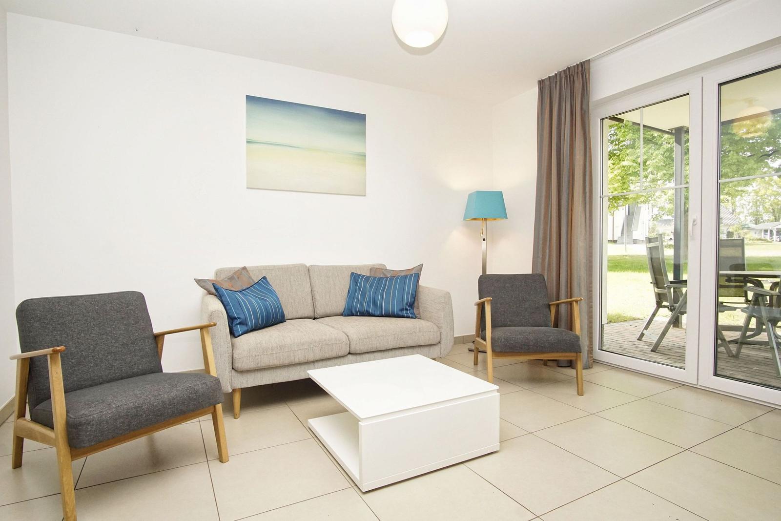 Wohnzimmer mit Sofa, zwei Sesseln, Tisch und Blick auf Terrasse.