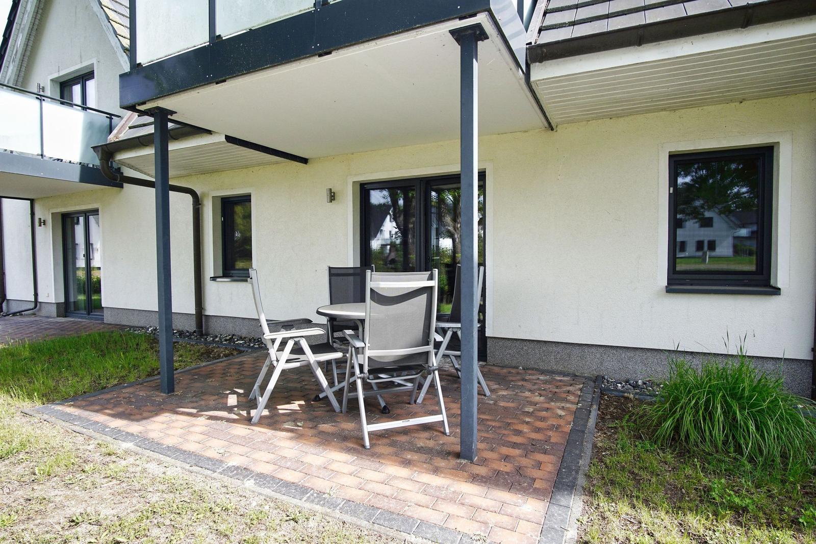 Terrasse mit Tisch und Stühlen unter Vordach. Haus mit Fenstern und Balkon.