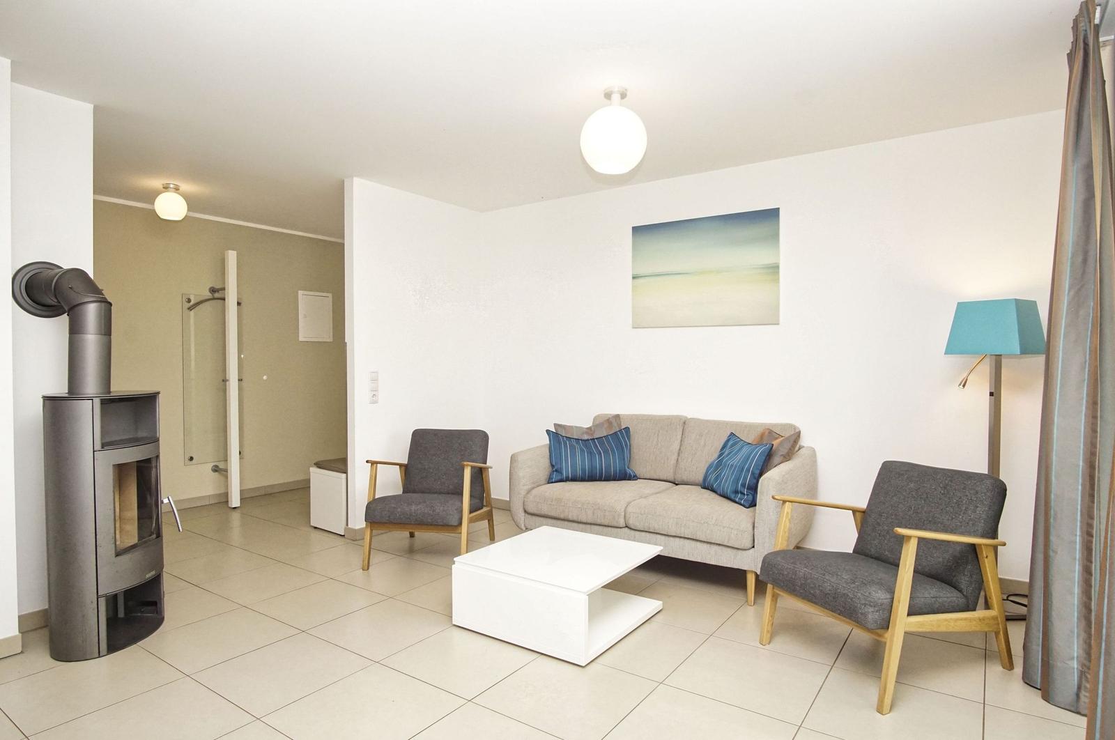 Wohnzimmer mit Sofa, zwei Sesseln, Kaminofen und moderner Beleuchtung.