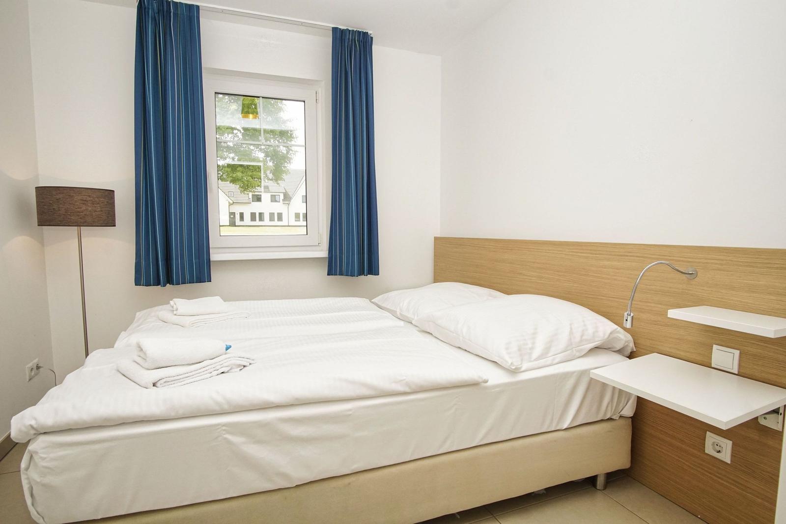 Ein Schlafzimmer mit einem Bett, blauen Vorhängen und einem Fenster mit Blick auf Gebäude.