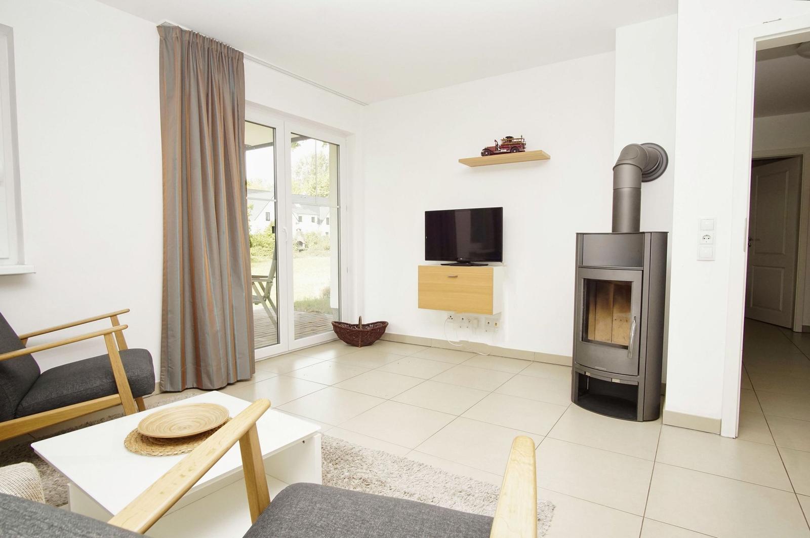 Wohnzimmer mit Holzofen, TV und Terrassentür. Möbel aus Holz und Stoff.
