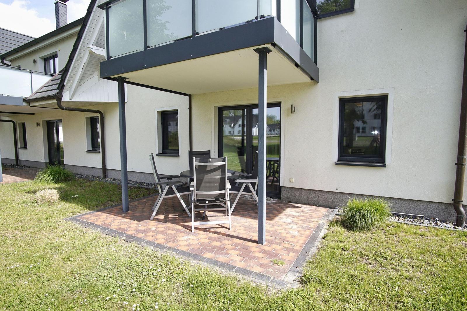 Terrasse mit Sitzgruppe und Glasbalcony an modernem Haus mit Garten.