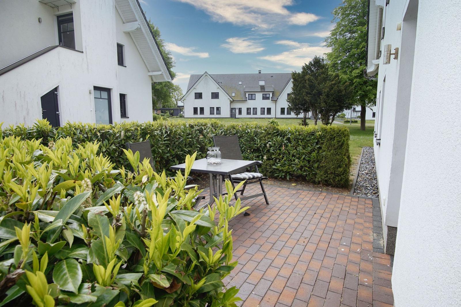 Terrace with table and chairs, surrounded by hedges and green areas.