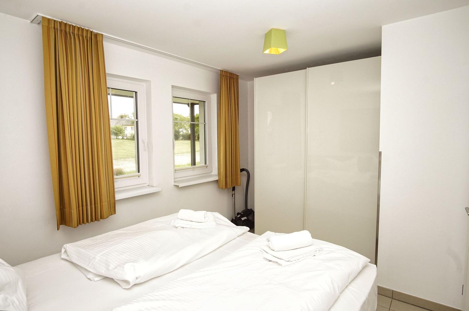 Room with double bed, two windows, and wardrobe. Curtains are yellow.