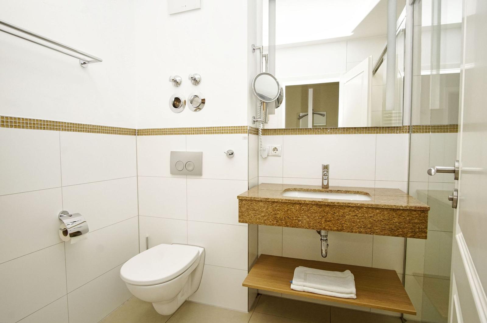 Bathroom with toilet, sink, and shower. Wall tiles and mirror visible.