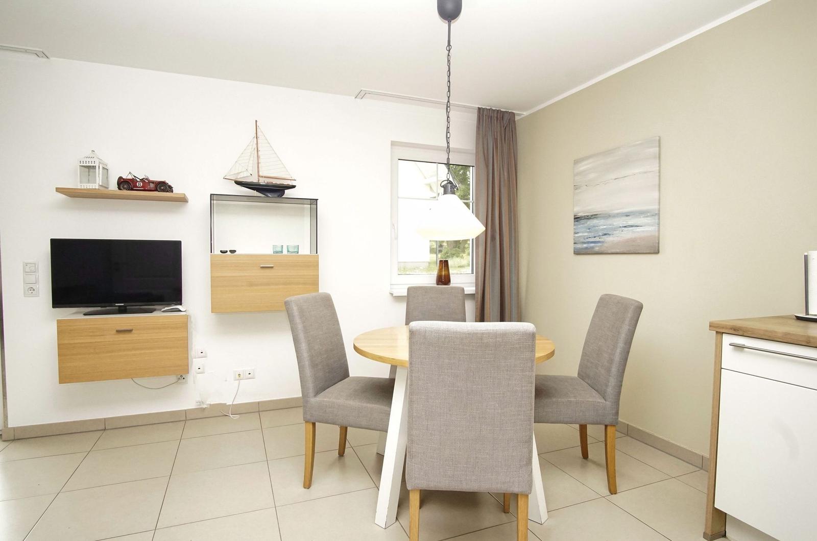 Dining area with round table and four chairs. Wall shelves and TV on the wall.