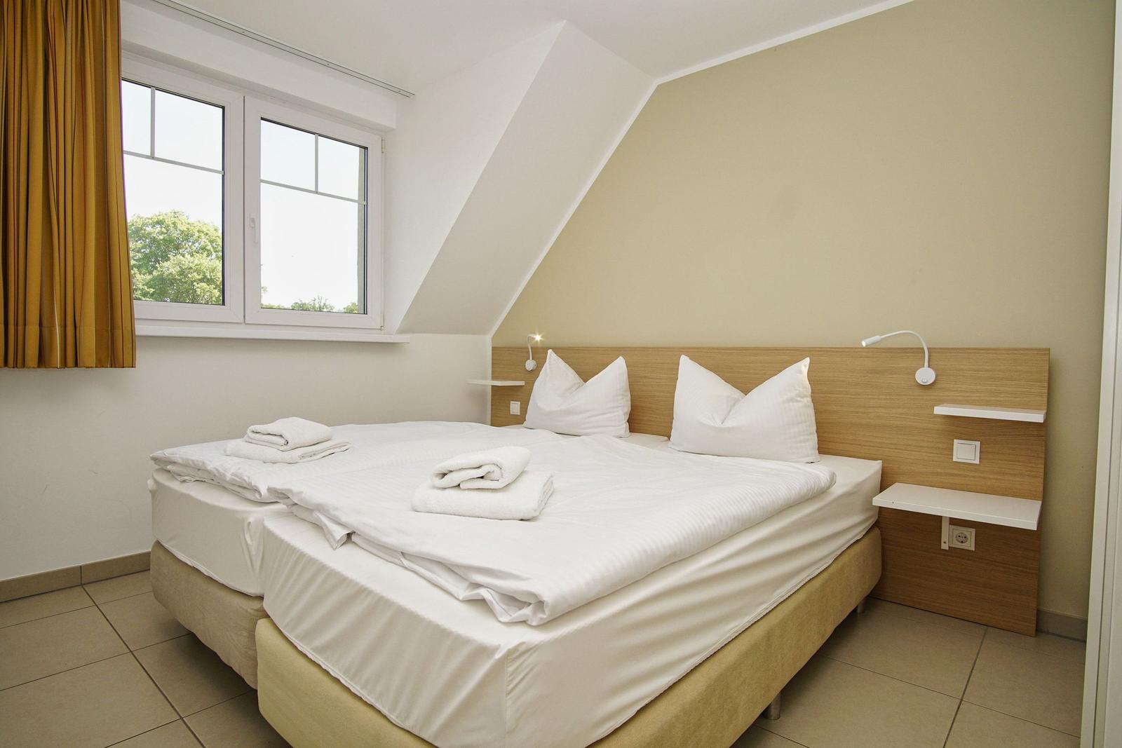 Doppelbett mit weißen Bettwäsche, Fenster mit gelben Vorhängen und Nachttische.