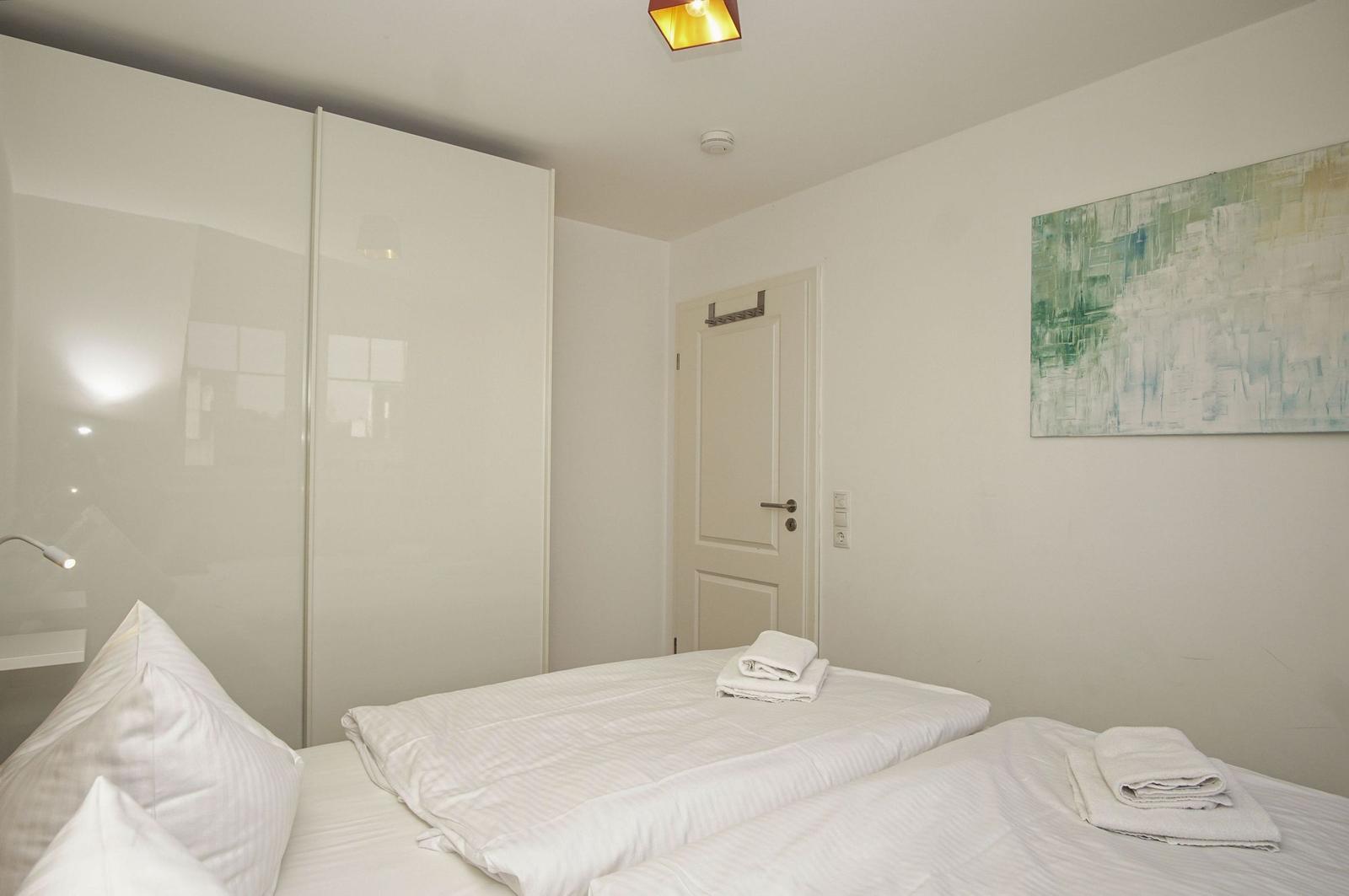 Schlafzimmer mit weißem Bett, Kleiderschrank und Wandbild.