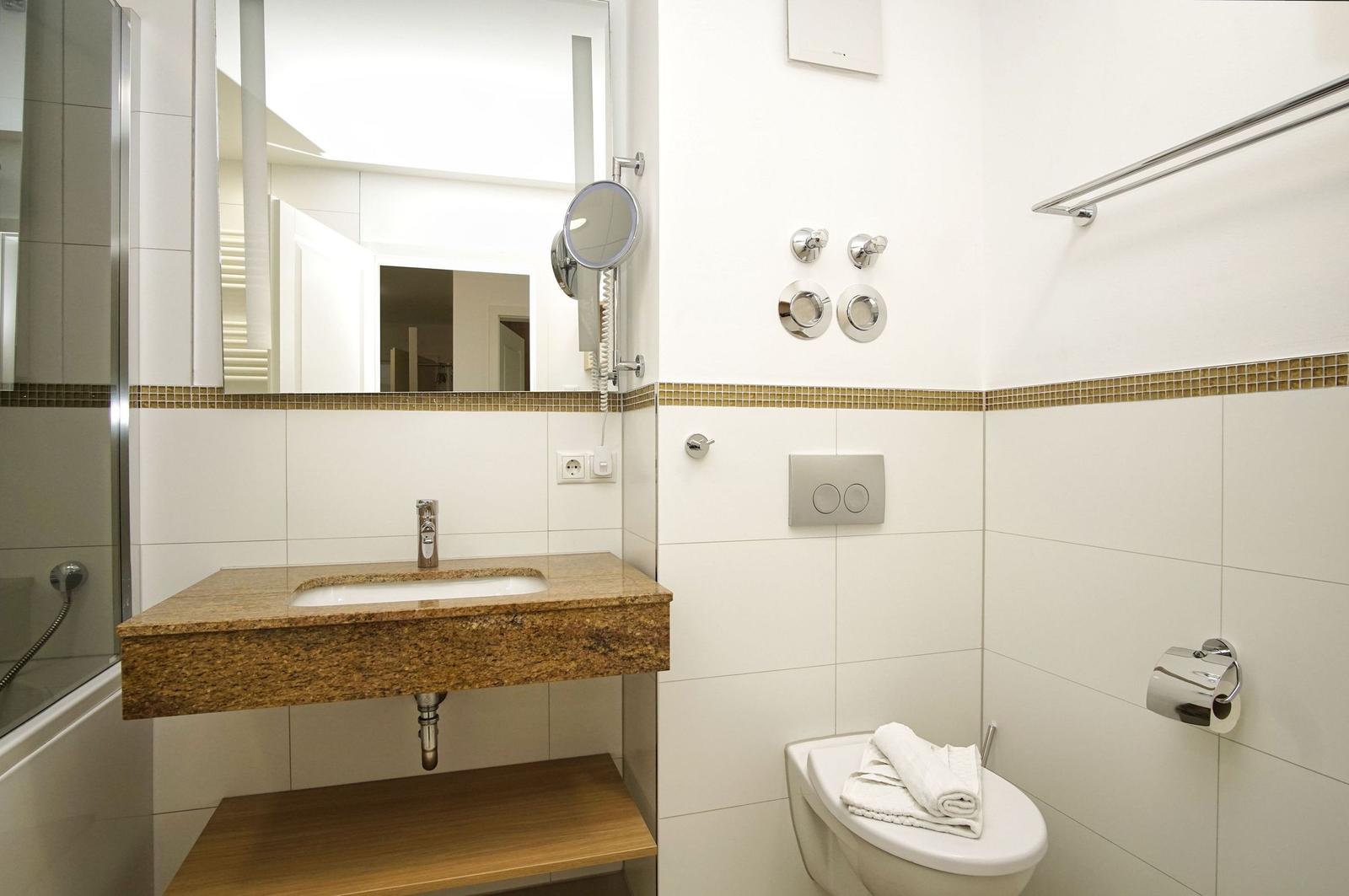Badezimmer mit Waschbecken, Spiegel und Toilette. Wandverkleidung mit Mosaikstreifen.