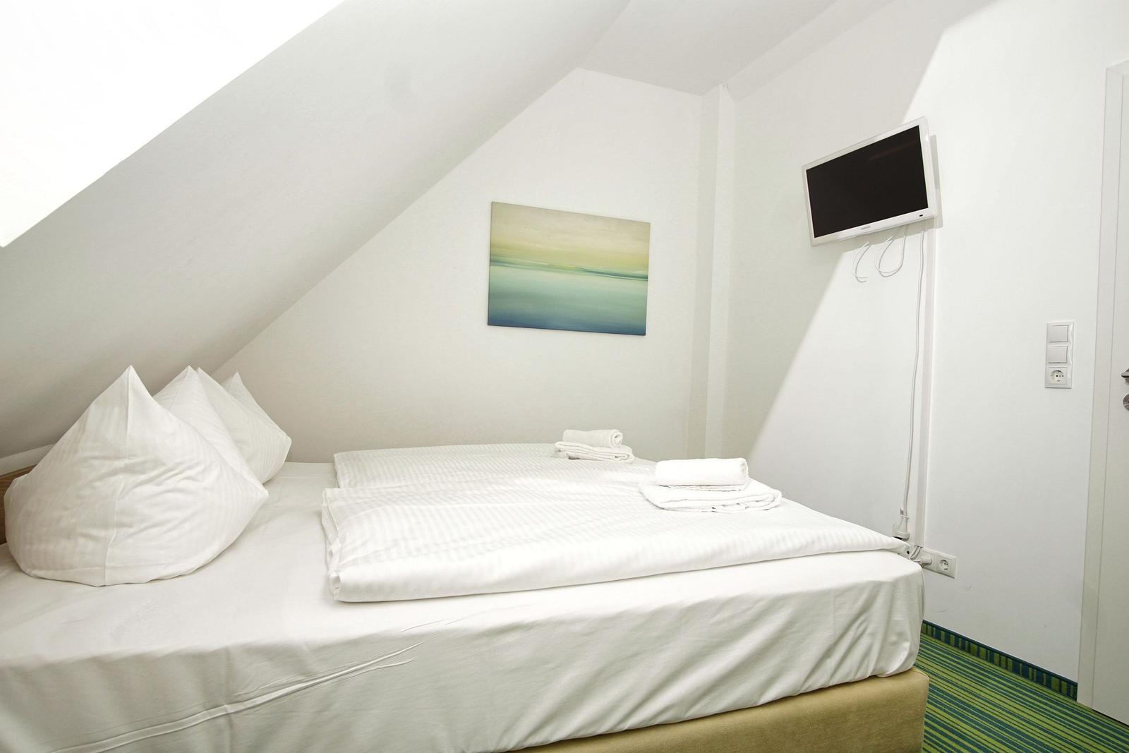 Schlafzimmer mit Doppelbett, Wandbild und Wand-TV unter Dachschräge.