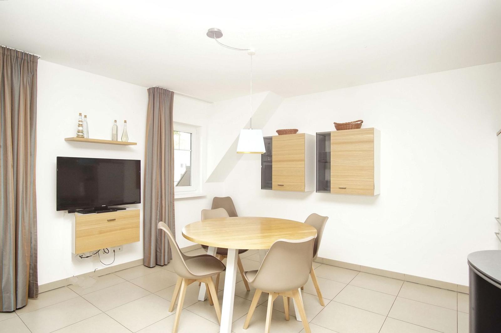 Esszimmer mit runden Tisch, Stühlen, Küchenschränken und Fernseher an der Wand.