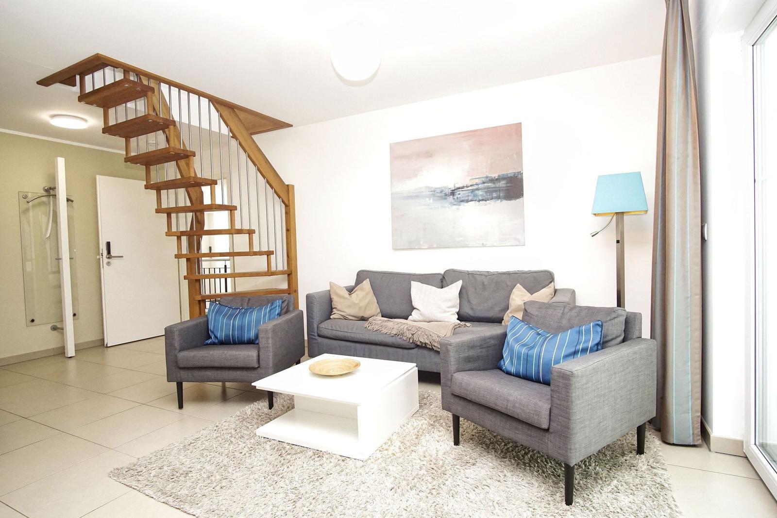 Wohnzimmer mit Sofa, zwei Sesseln und Treppe zur oberen Etage.