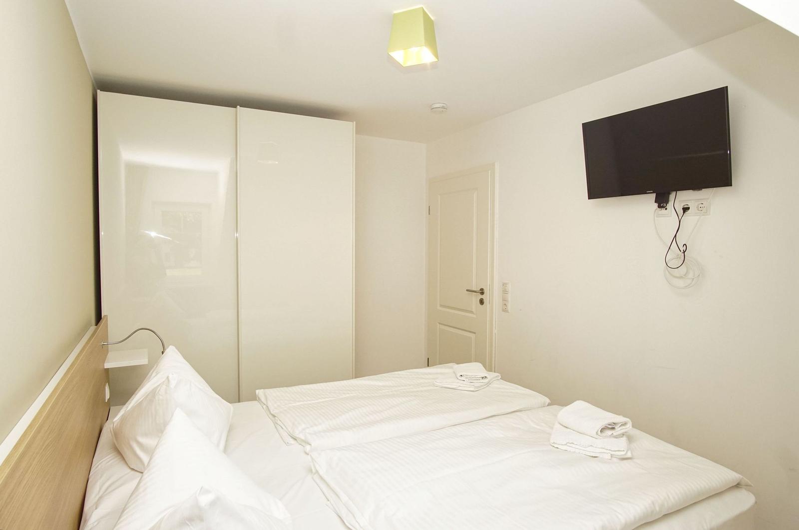 Schlafzimmer mit Bett, Kleiderschrank und Wandfernseher.