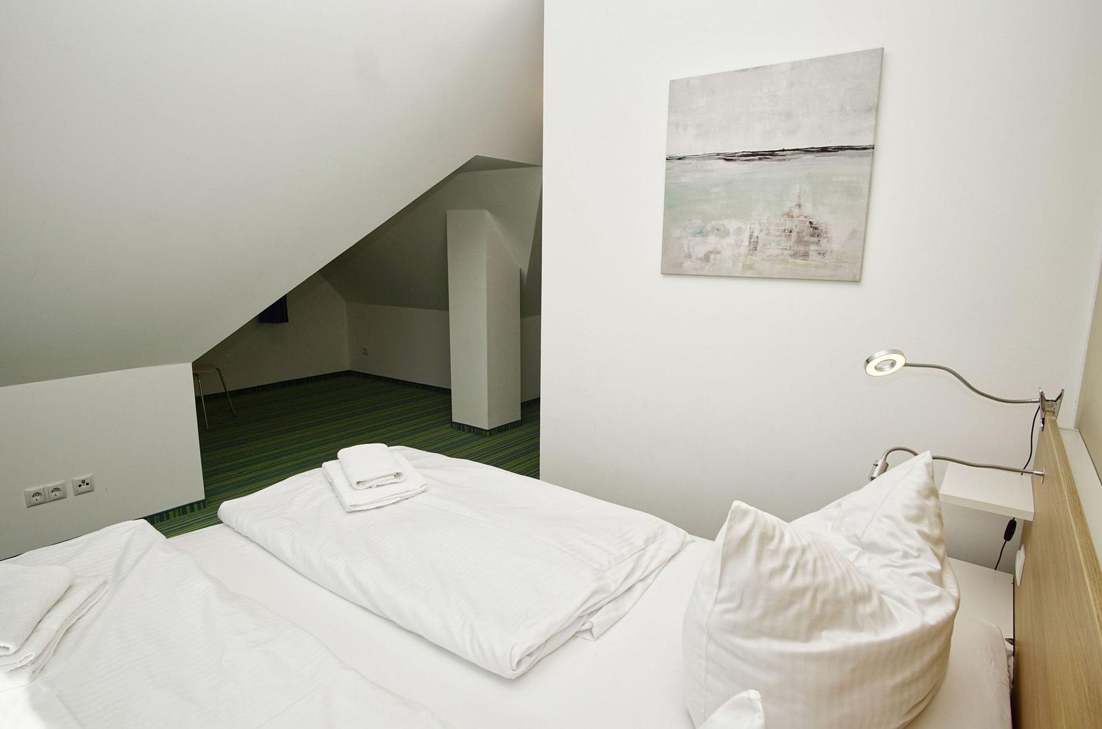 Schlafzimmer mit Dachschräge, Bett, Wandbild und Nachttischlampe.