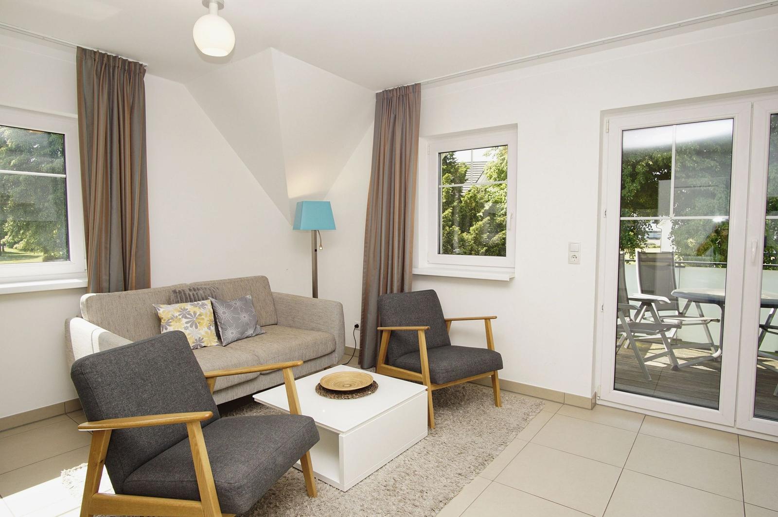 Wohnzimmer mit Sofa, zwei Sesseln und Glastür zur Terrasse.