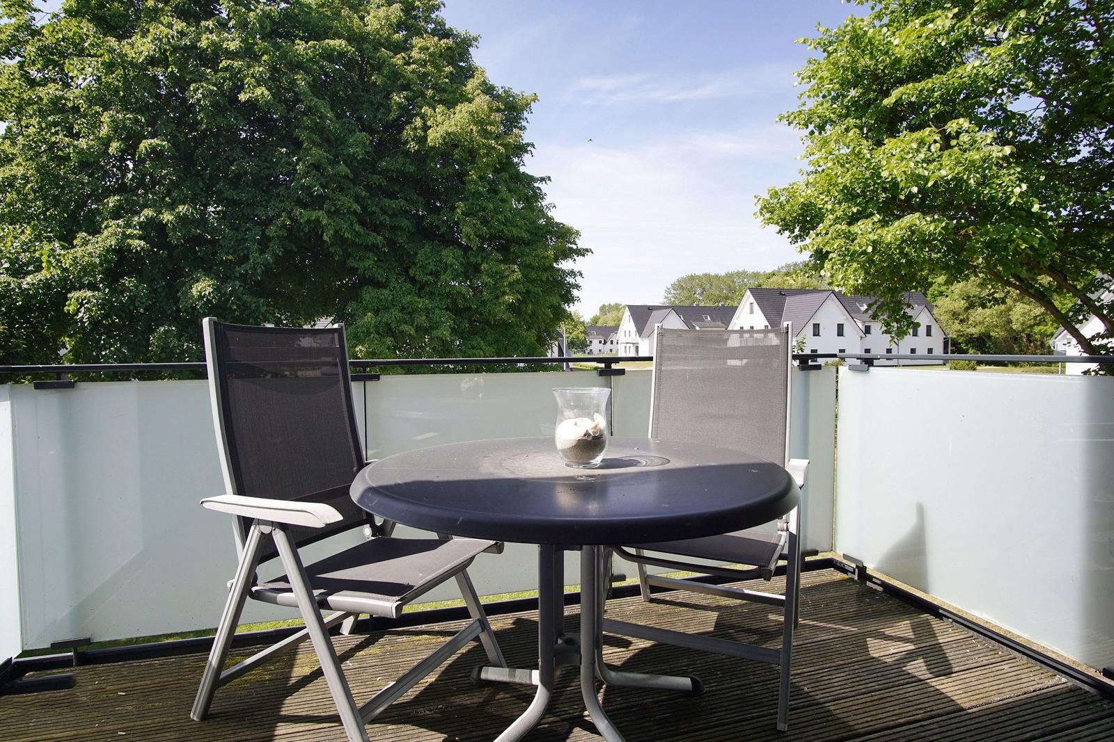 Terrasse mit Tisch und zwei Stühlen, Blick auf grüne Bäume und weiße Häuser.