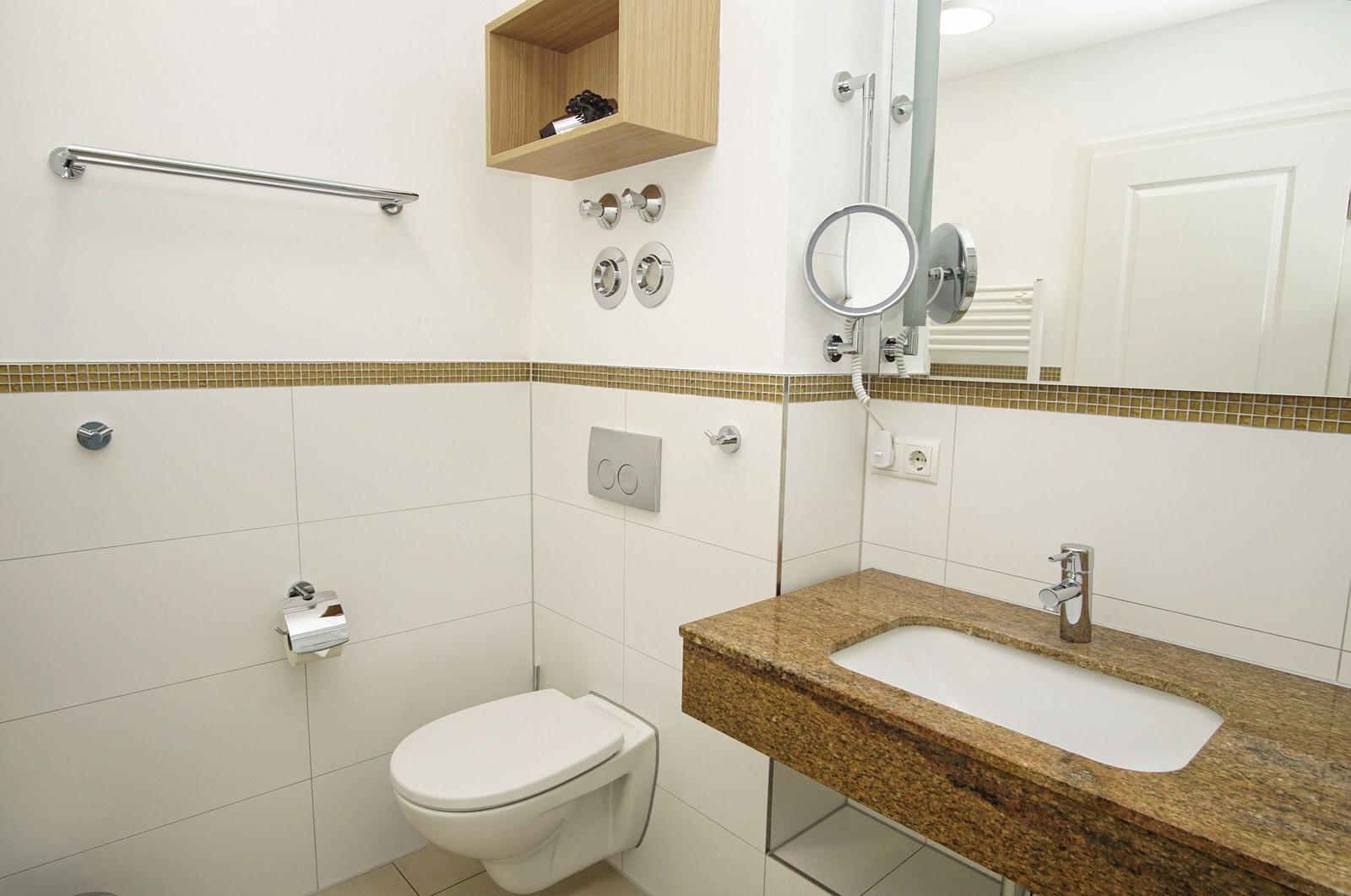 Bathroom with toilet, sink, and mirror. Wooden shelf and chrome fixtures.