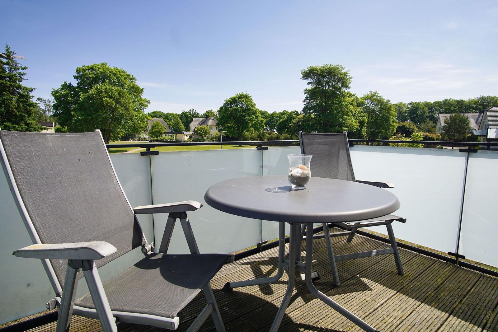 Terrace with table and two chairs, view of green trees and houses.