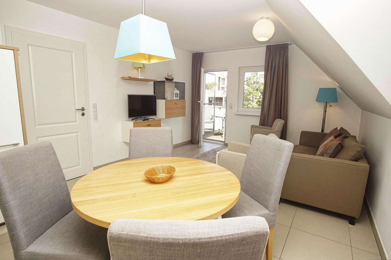 Living and dining area with round table, sofa, and TV. Balcony via sliding door.