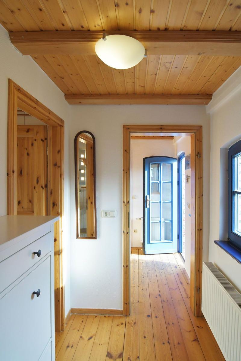 Hausflur mit Holzdecke, -boden und -türen. Spiegel, Fenster und Schrank sichtbar.