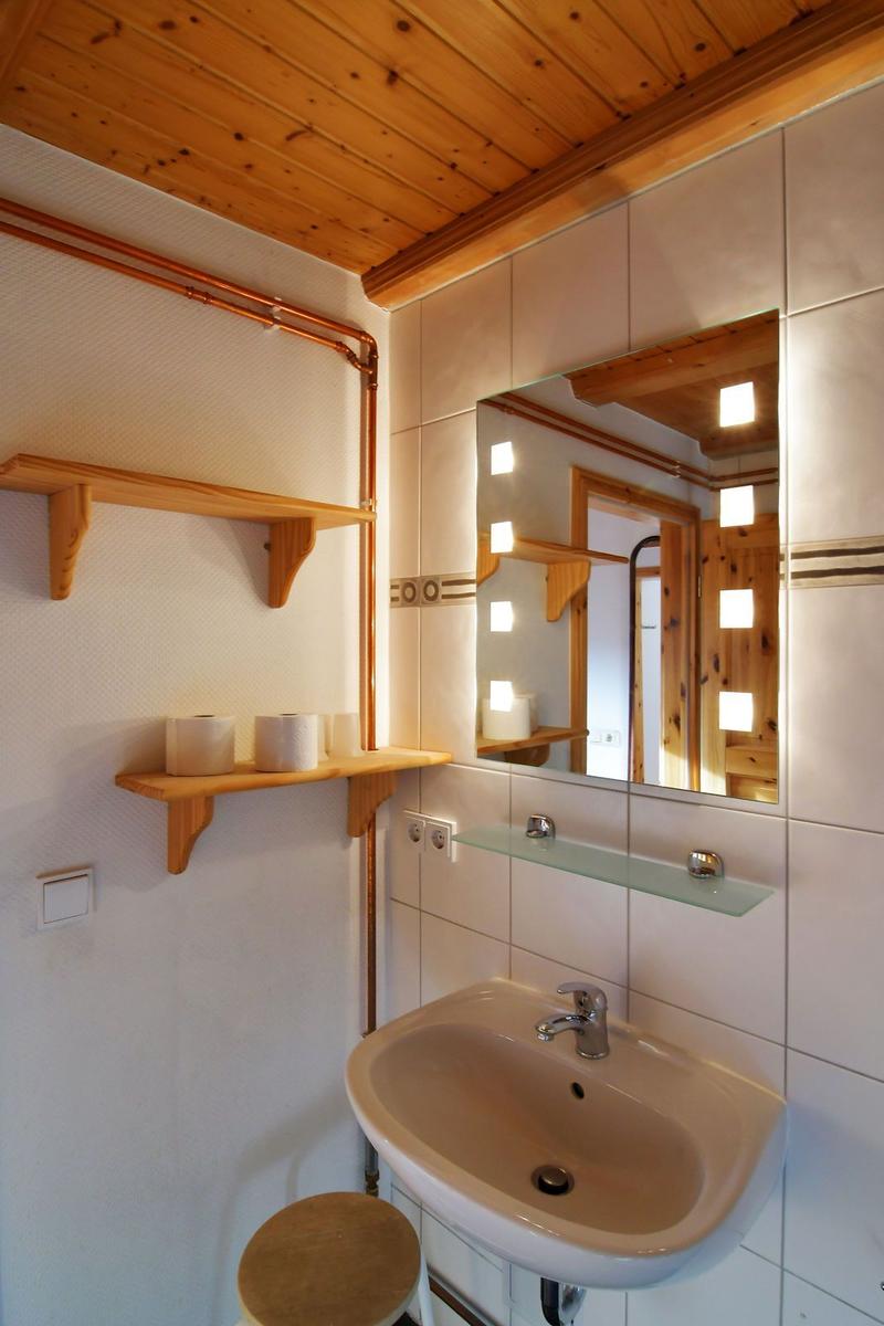 Badezimmer mit Waschbecken, Spiegel und Holzregalen an der Wand.