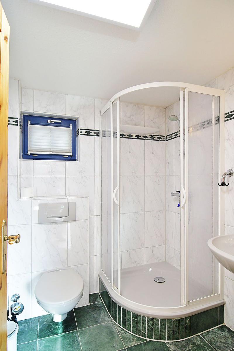 Badezimmer mit Dusche, Toilette und Waschbecken. Wandfliesen und grüner Bodenbelag.