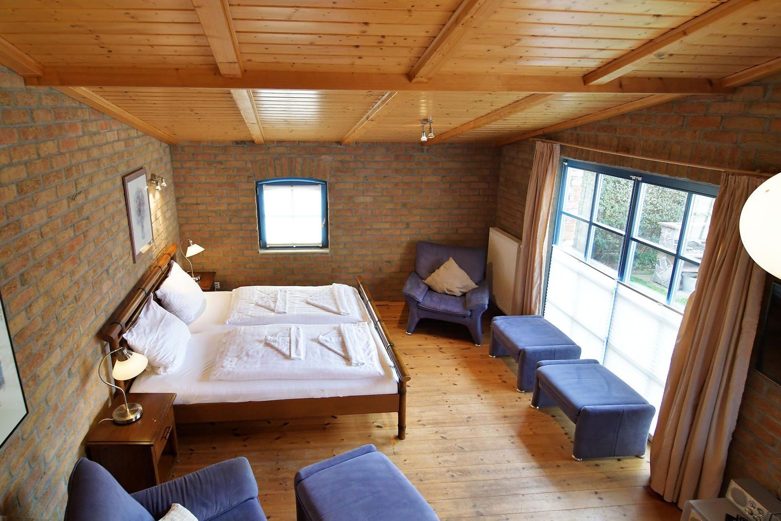 Schlafzimmer mit Holzboden, Backsteinwänden und Doppelbett mit blauen Sesseln.
