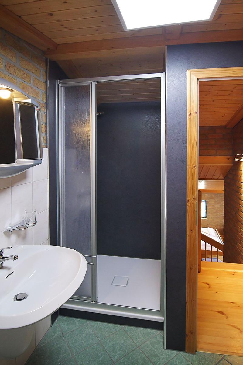 Badezimmer mit Dusche, Waschbecken und Holzdecke.