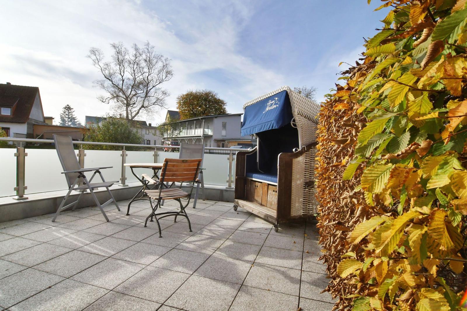 Terrasse mit Liegestuhl, Tisch und Stühlen, Blick auf Wohnhäuser und Bäume.