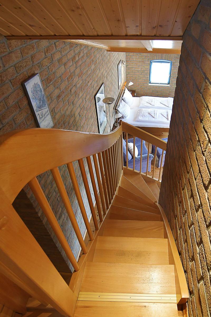 Holzstufen führen zu einem Schlafzimmer mit Bett und Fenster.
