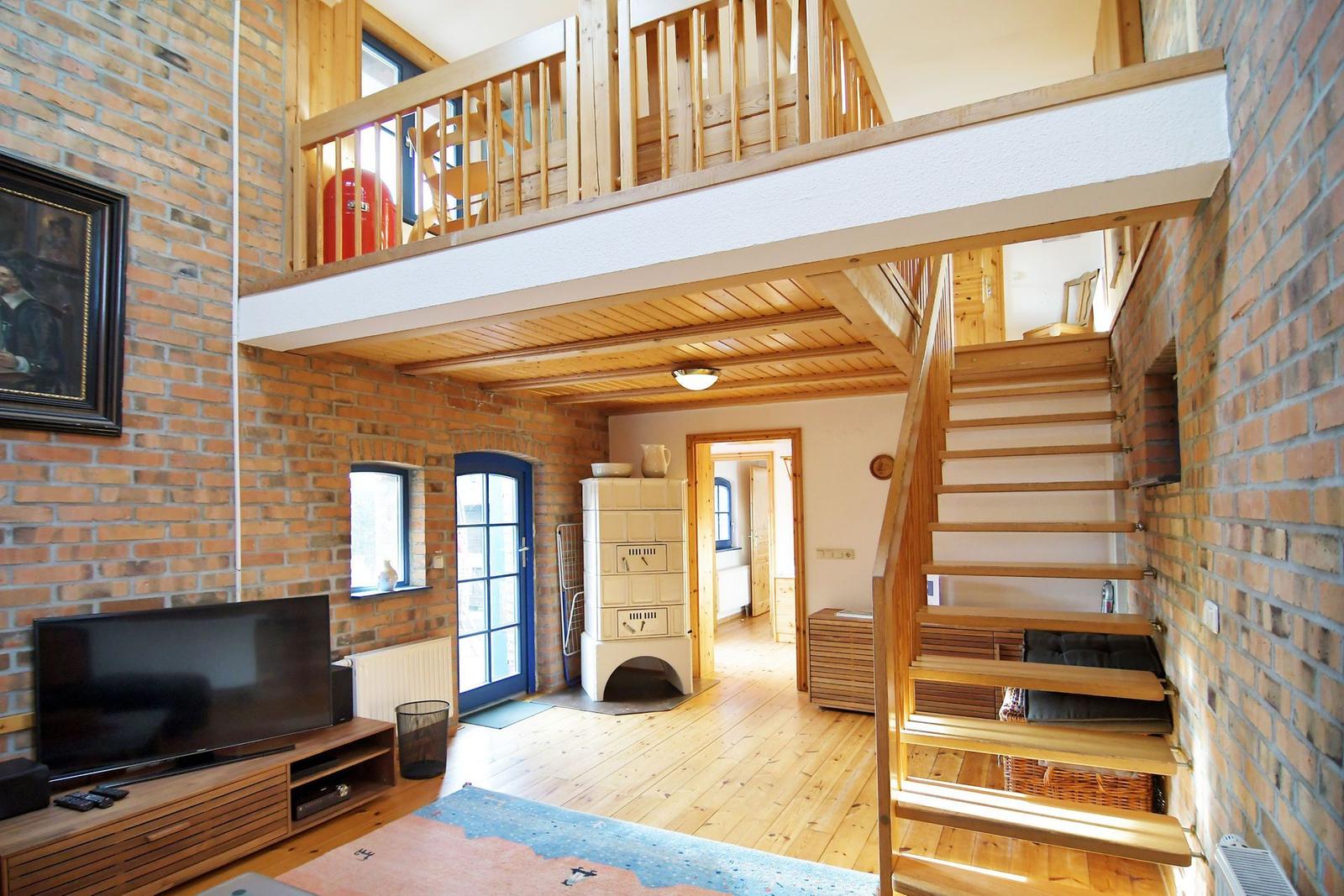 Wohnraum mit Holzstufen, Balkon und Kaminofen an der Wand.
