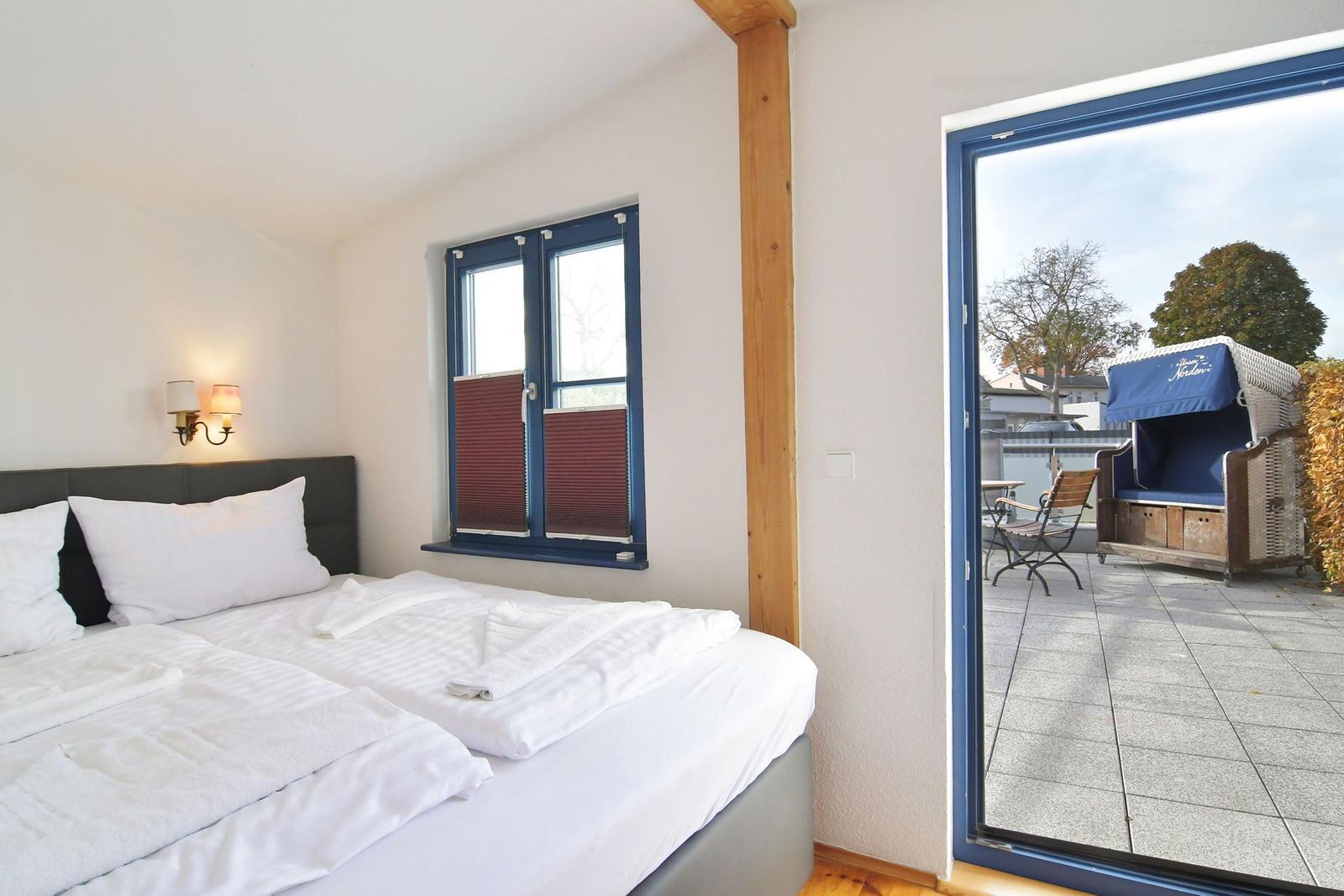 Schlafzimmer mit Doppelbett, Fenster und Zugang zur Terrasse mit Strandkorb.