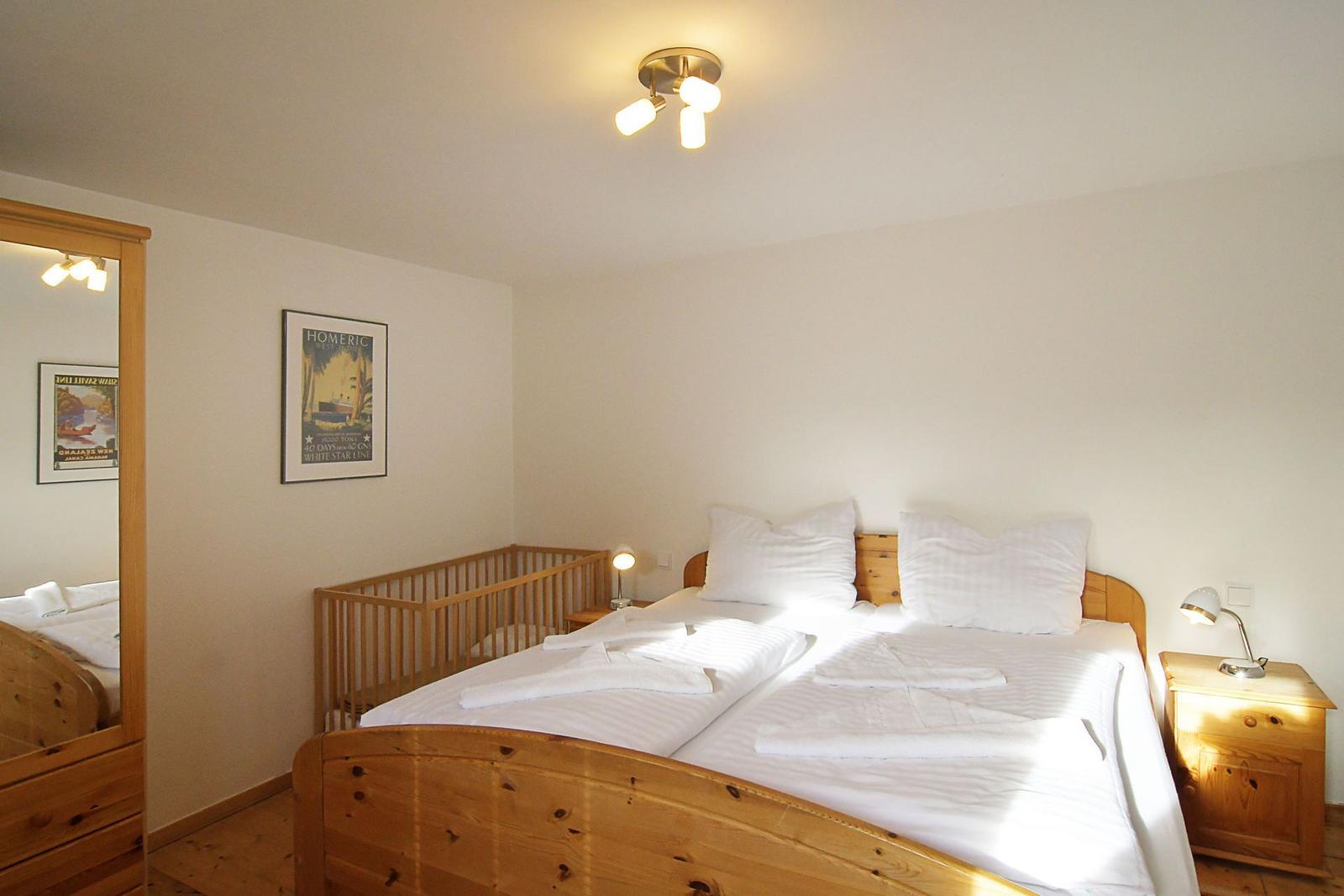 Schlafzimmer mit Holzbett, Babybett, Nachttisch und Wandbild.