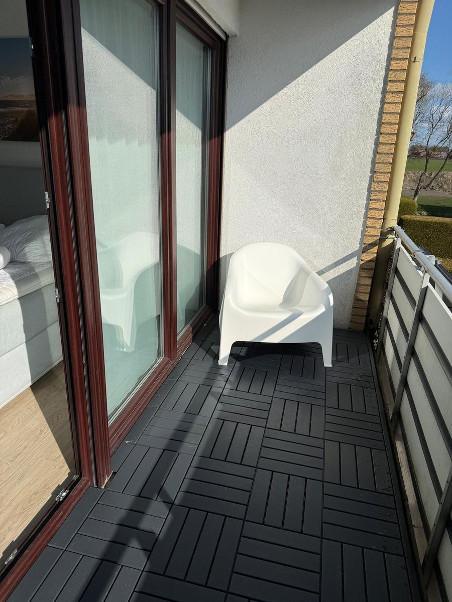 Terrasse mit weißem Stuhl und schwarzen Bodenplatten. Durch Glastüren ist Schlafzimmer sichtbar.