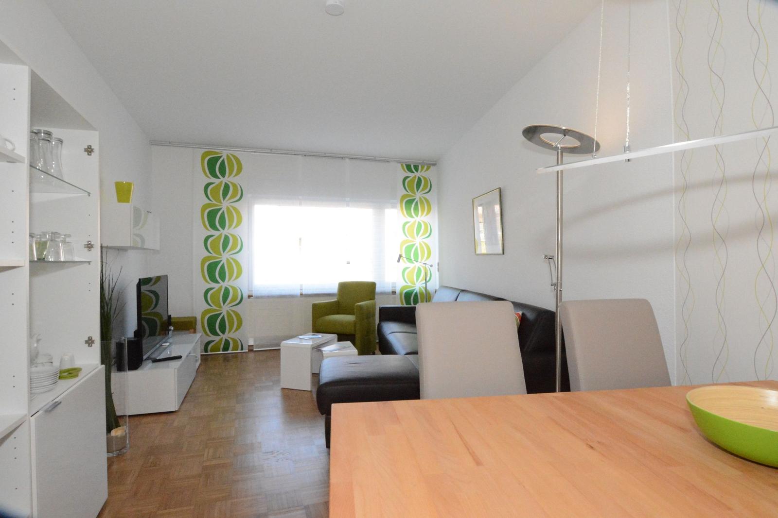 Wohn- und Essbereich mit Sofa, Stühlen und Fenster mit grün-gelben Vorhängen.