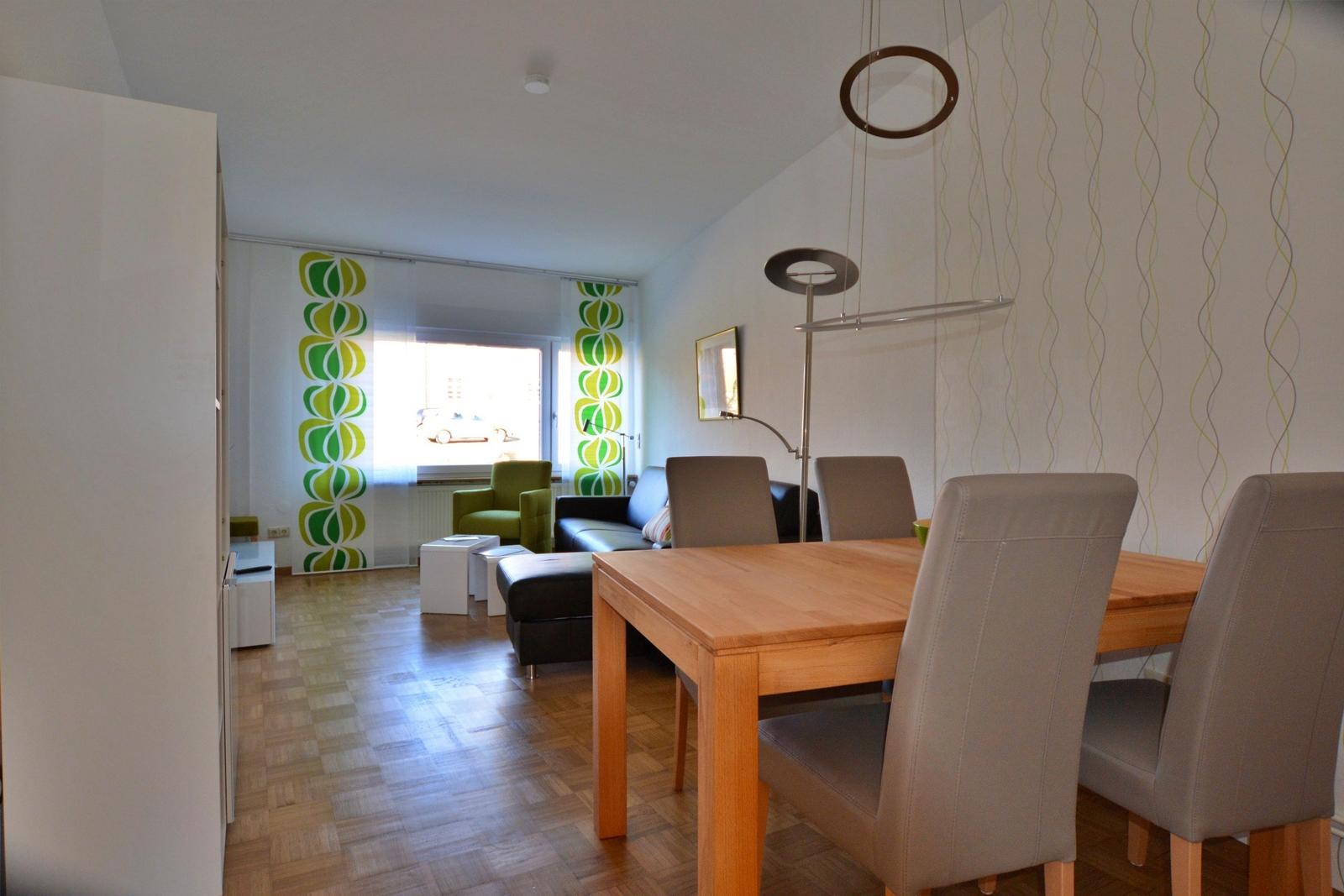 Essbereich mit Holztisch und Stühlen. Wohnbereich mit Sofa und grüner Sitzgelegenheit.