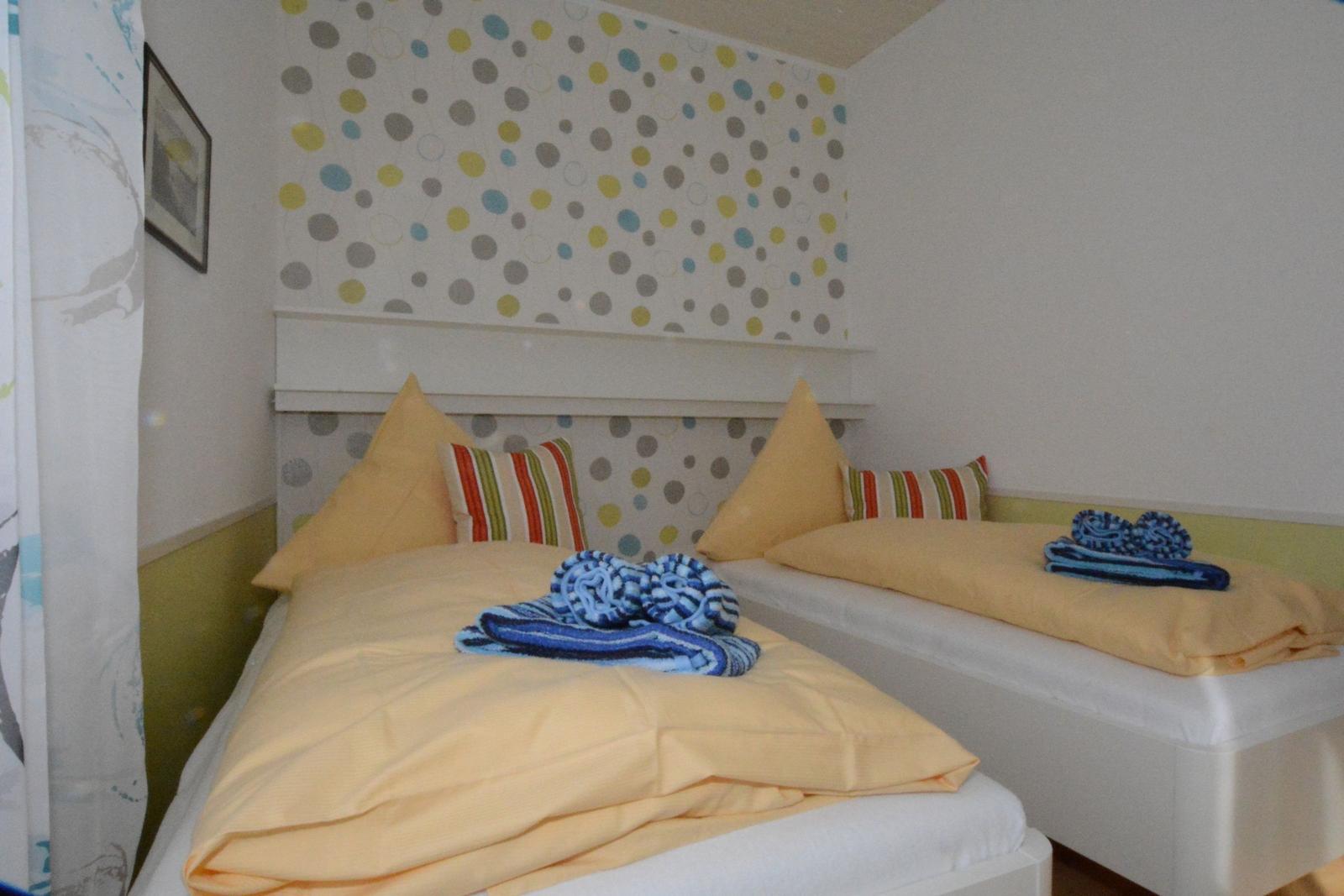 Zwei Betten mit gelben Bettwäsche und gestreiften Kissen. Wand mit bunten Punkten.